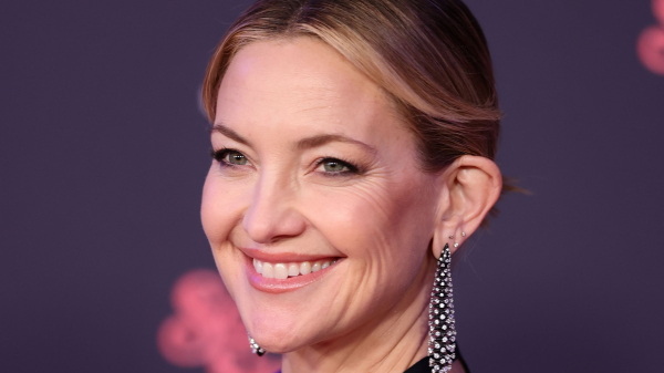 Kate Hudson appears at a premiere in a blue dress. She wears her hair back and wears long earrings.