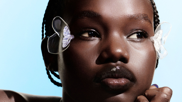 A closeup shot of a darkskinned model with glowing skin wearing makeup accessories on the outside of both eyes